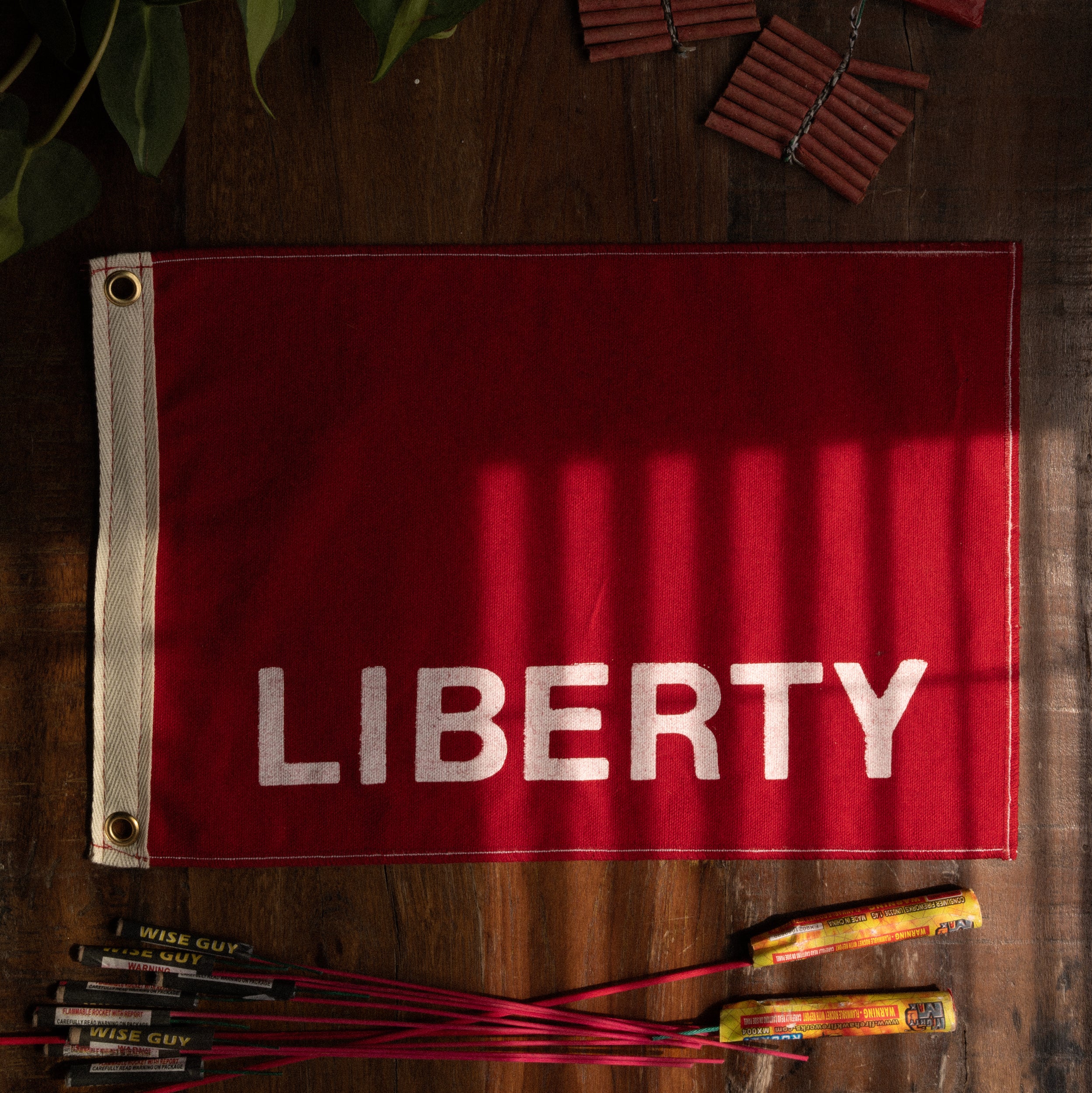 Red flag with 'LIBERTY' printed on it, surrounded by fireworks on a wooden surface.